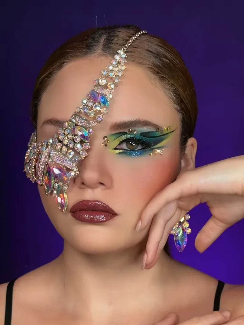 Maquillaje editorial con joyería sobre el rostro y delineado verde esmeralda