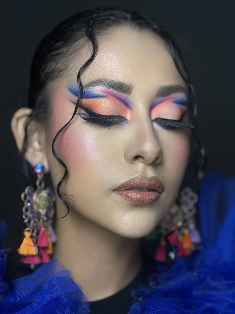 Maquillaje de color naranja y azul con delineado gráfico y piel pulida